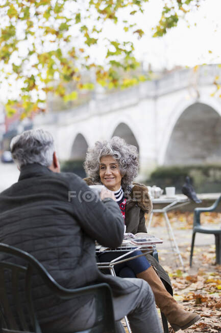 Улыбающаяся активная пожилая пара, наслаждающаяся кофе в кафе в осеннем парке — стоковое фото