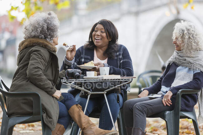 Laughing active senior women friends sharing dessert at autumn park cafe — Stock Photo