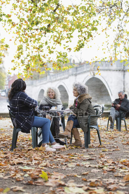 Sonriendo activo senior mujeres amigos disfrutando de café en otoño parque cafetería - foto de stock