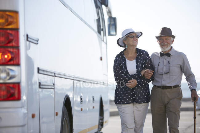 Sonriendo activa pareja de turistas mayores caminando a lo largo de autobús - foto de stock
