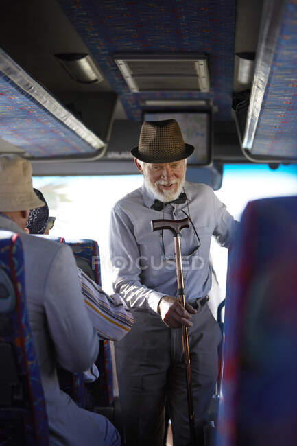 Активный пожилой человек в шляпе с тростью садится в экскурсионный автобус — стоковое фото