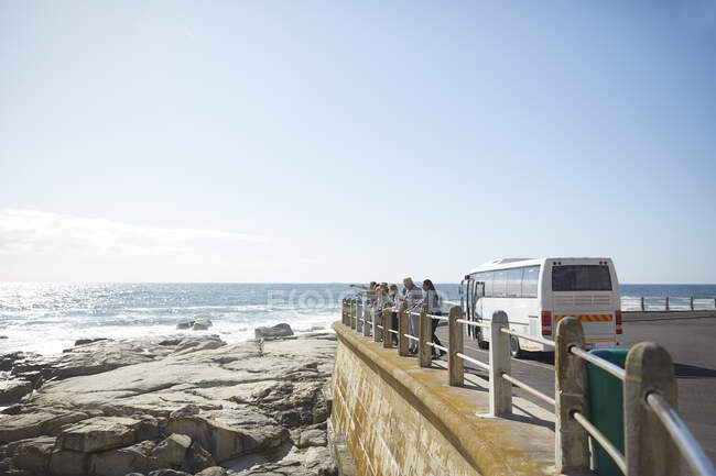 Туристи, які дивляться на сонячний вид на океан за межами туристичного автобуса — стокове фото