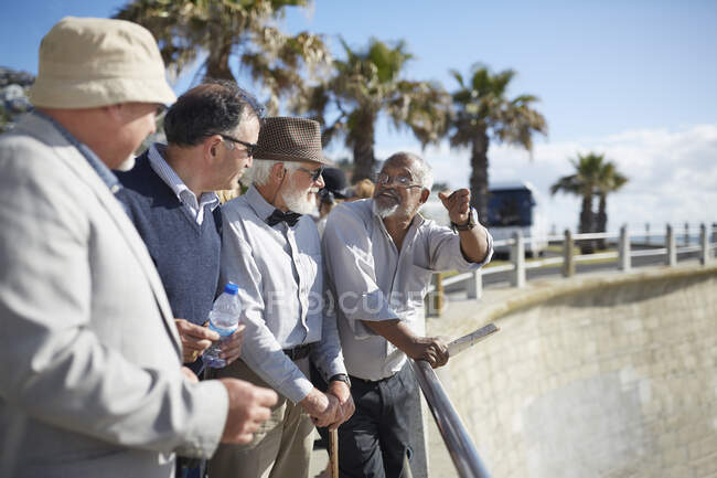 Активные старшие друзья-туристы разговаривают на солнечной набережной — стоковое фото