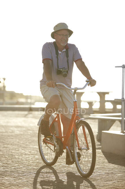 Homem idoso ativo bicicleta turística equitação no calçadão ensolarado — Fotografia de Stock