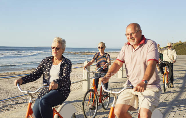 Amici turistici anziani attivi in bicicletta sul lungomare soleggiato lungo l'oceano — Foto stock