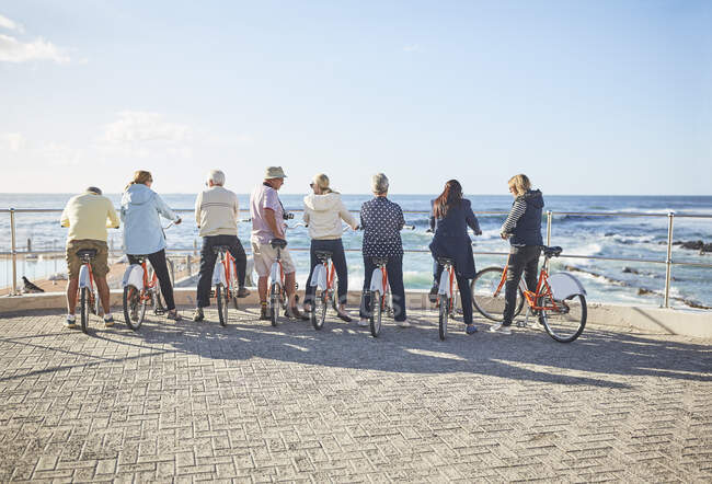 Активные старшие друзья-туристы на велосипедах смотрят на солнечный вид на океан — стоковое фото