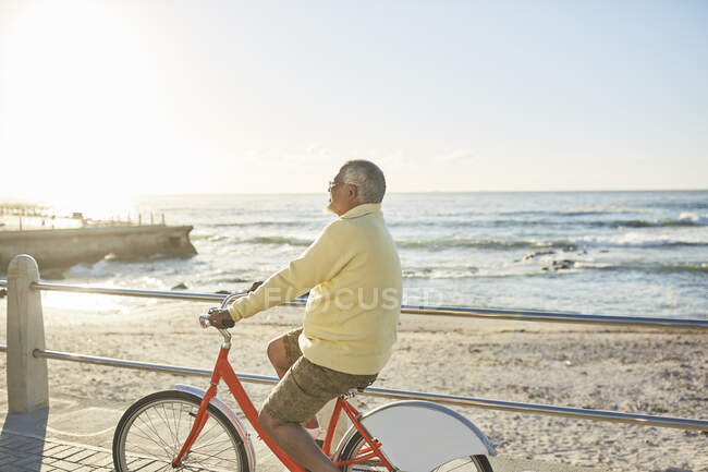 Active senior man tourist bike riding on sunny boardwalk along ocean — Stock Photo