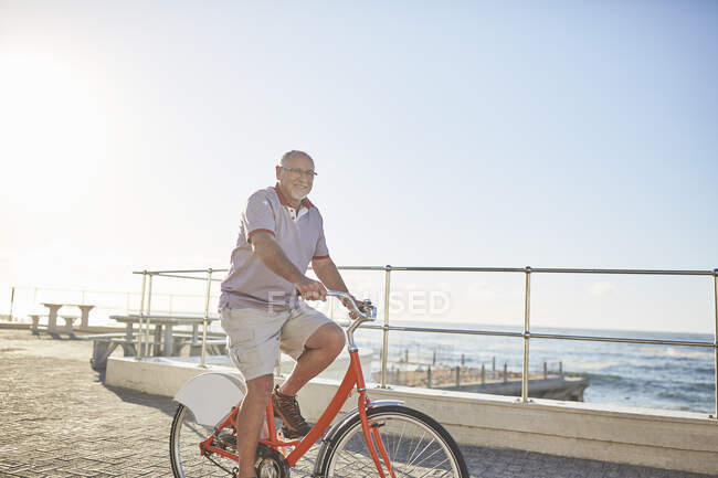 Active senior man tourist bike riding on sunny boardwalk along ocean — Stock Photo