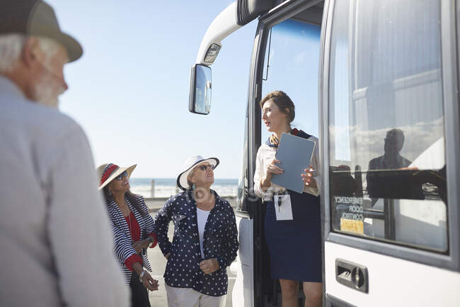 Tour guide talking to active senior tourists at doorway of tour bus — Stock Photo