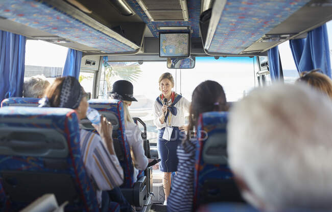 Guida turistica femminile con microfono che parla con i turisti anziani attivi sul bus turistico — Foto stock