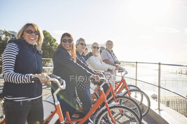 Portrait smiling, confident active senior tourist friends on bicycles on sunny boardwalk — Stock Photo