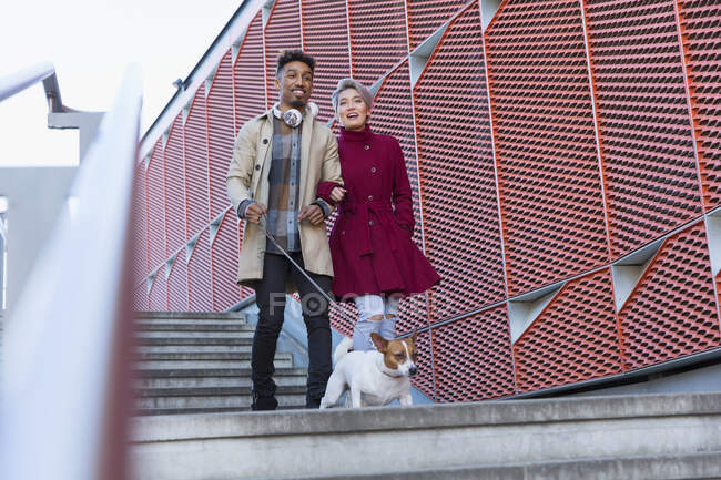 Sorrindo jovem casal andando cão baixo urbano, escadas modernas — Fotografia de Stock