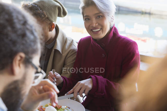 Retrato sonriente mujer joven comiendo con amigos en el restaurante - foto de stock