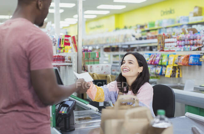 Cajero sonriente dando recibo al cliente en la caja del supermercado - foto de stock