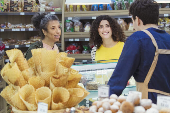 Mujeres hablando con el trabajador en la vitrina de la panadería en el supermercado - foto de stock