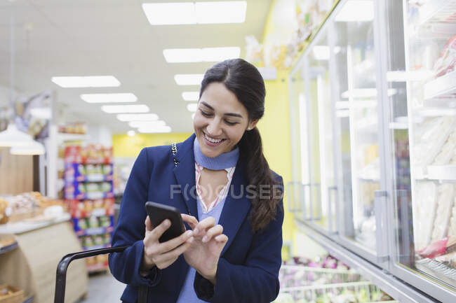 Улыбающаяся женщина с магазинами смартфонов в супермаркете — стоковое фото