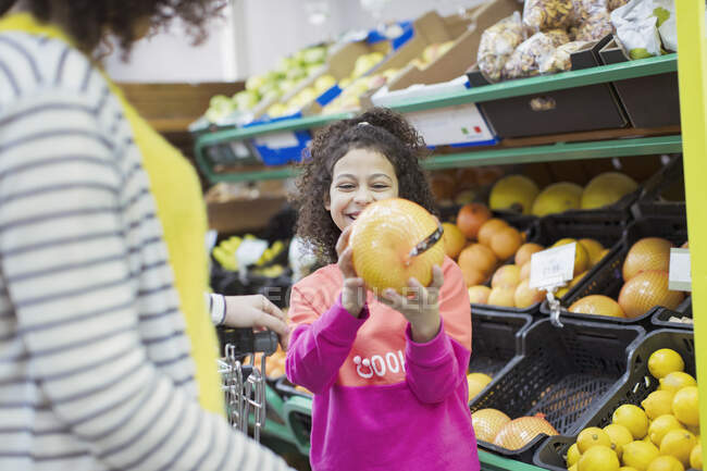 Улыбающаяся дочь показывает грейпфрут матери в супермаркете — стоковое фото