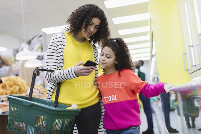 Mother and daughter with smart phone shopping in supermarket — Stock Photo
