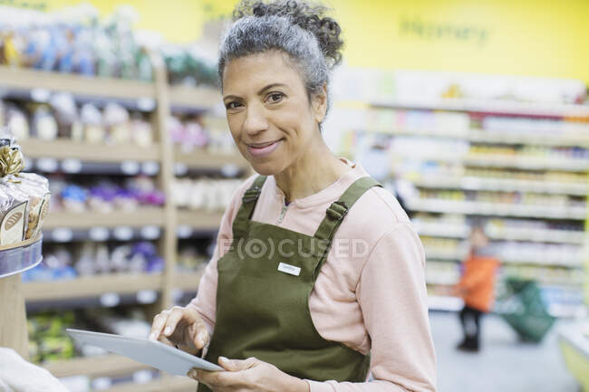 Portrait smiling, confident female grocer with digital tablet working in supermarket — Stock Photo