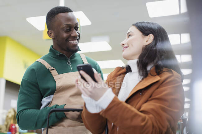 Grocer ajudando o cliente com telefone inteligente no supermercado — Fotografia de Stock