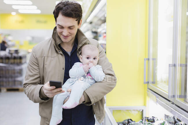 Отец с дочкой проверяет смартфон, делает покупки в супермаркете — стоковое фото