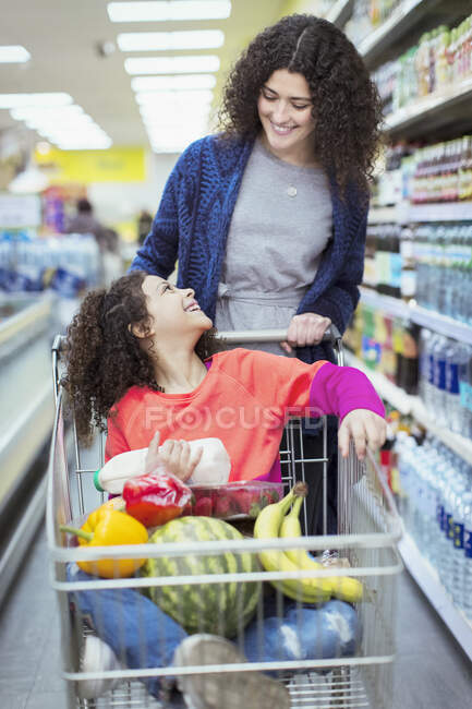 Felice madre spingendo figlia nel carrello della spesa nel supermercato — Foto stock