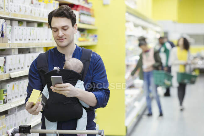 Father with baby scanning label on box in supermarket — Stock Photo