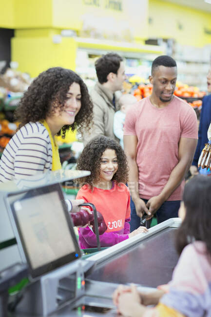 Cashier helping mother and daughter at supermarket checkout — Stock Photo