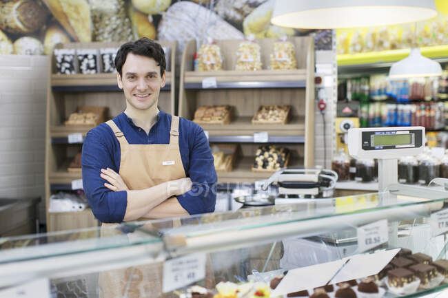 Retrato confiado trabajador masculino detrás de la vitrina de panadería en el supermercado - foto de stock