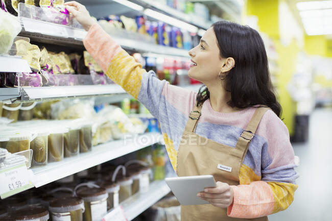 Comedero femenino con tableta digital trabajando en el supermercado - foto de stock