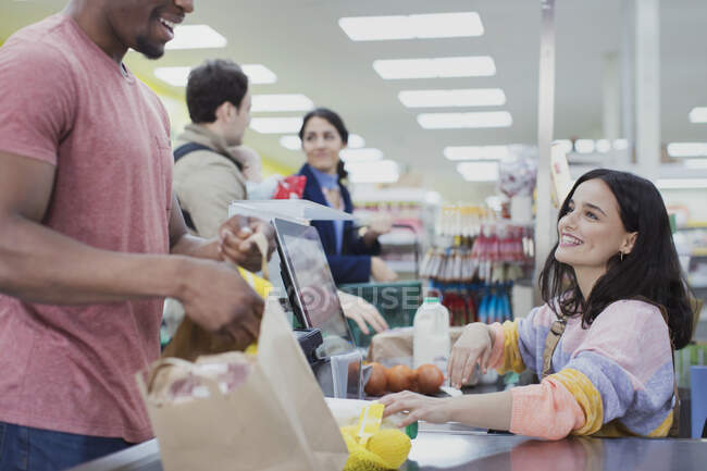 Friendly cashier helping customers at supermarket checkout — Stock Photo