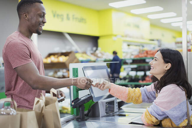 Cashier giving receipt to customer at supermarket checkout — Stock Photo