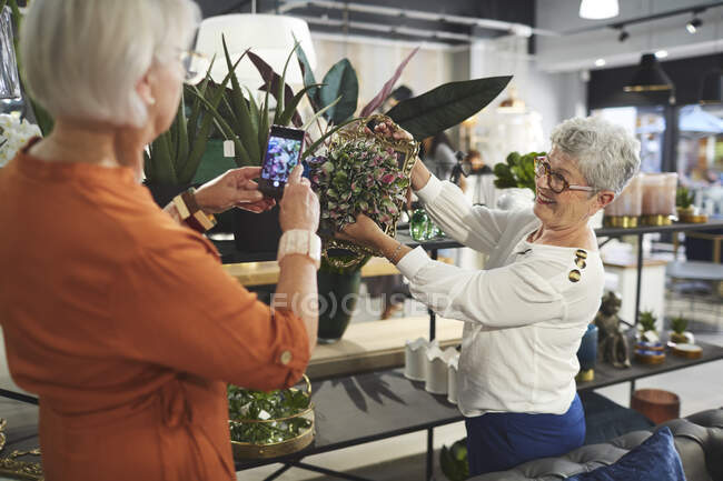 Las mujeres mayores con el teléfono de la cámara en la tienda de decoración del hogar - foto de stock
