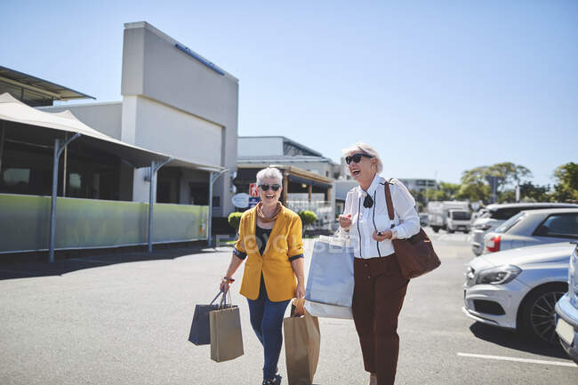 Mujeres mayores felices con bolsas de compras en el estacionamiento soleado - foto de stock