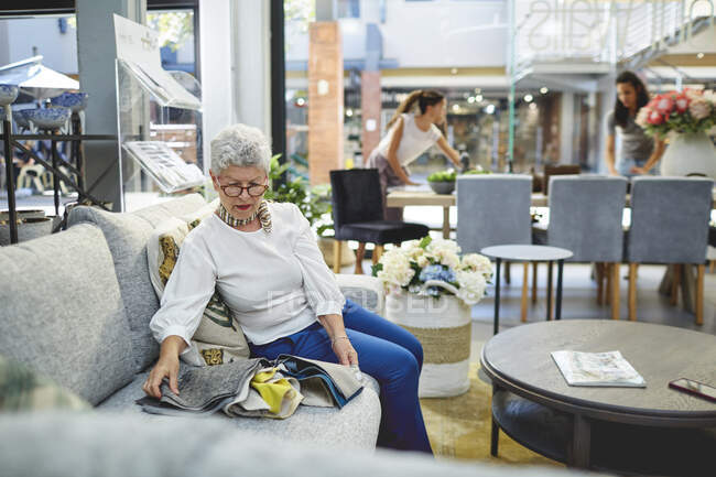 Старша жінка дивиться на тканину на дивані в магазині декору. — стокове фото