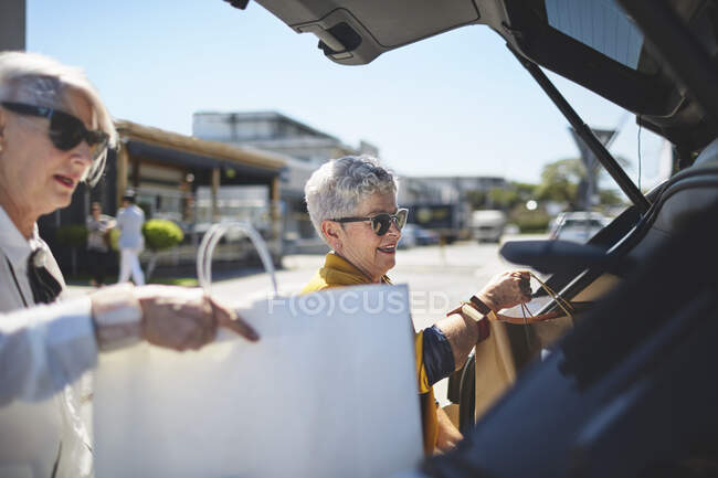 Seniorin lädt Einkaufstüten auf sonnigem Parkplatz in Auto — Stockfoto