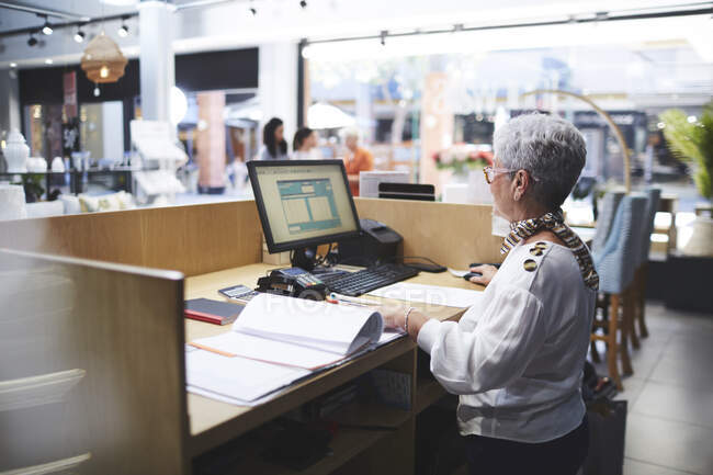 Senior woman working at computer in home decor shop — Stock Photo