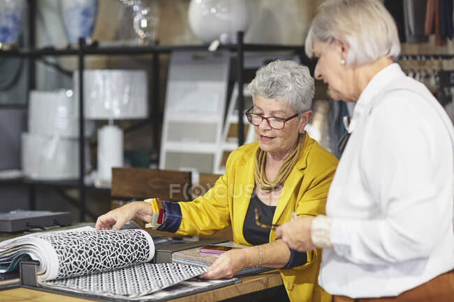 Mujeres mayores mirando muestras de tela en la tienda de decoración del hogar - foto de stock