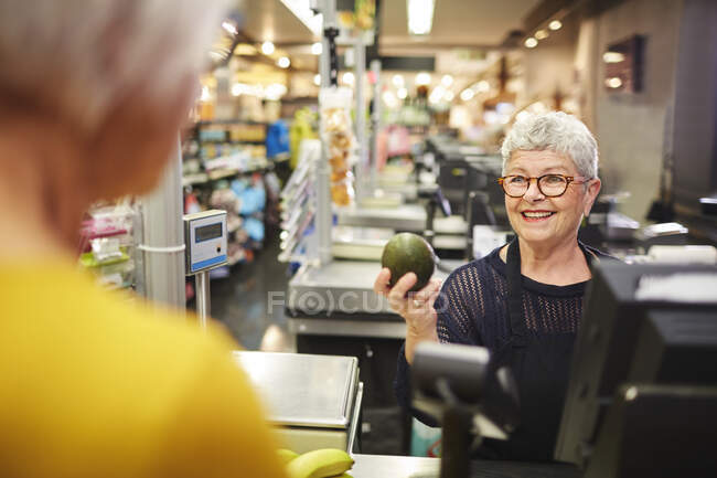 Smiling senior female cashier helping customer at grocery checkout — Stock Photo