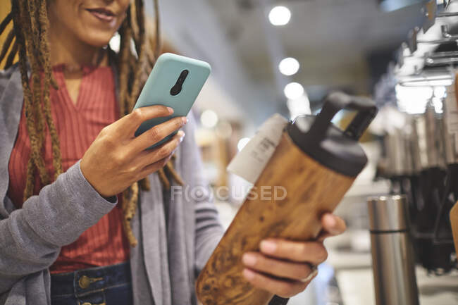 Donna con smart phone fotografare bottiglia isolata in negozio — Foto stock