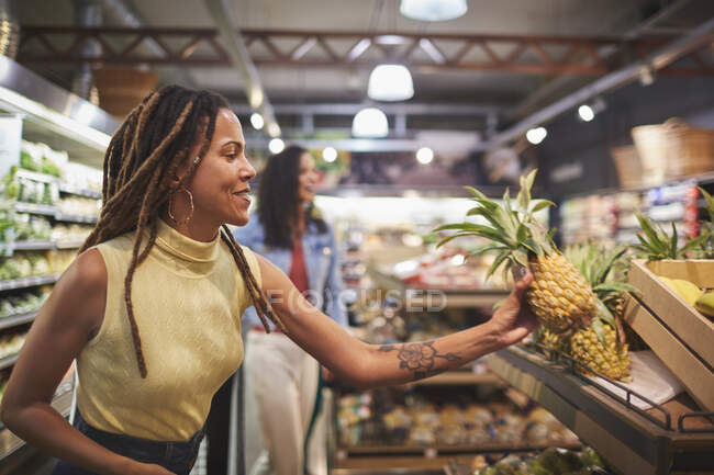 Woman shopping for pineapple in supermarket produce section — Stock Photo