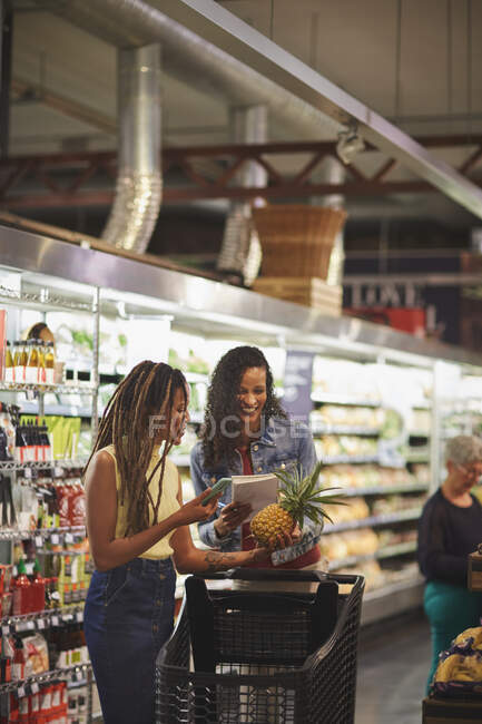 Жінки зі списком покупок та покупками смартфонів у супермаркеті — стокове фото