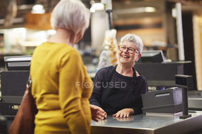 Felice senior cassiere saluto cliente al checkout supermercato — Foto stock