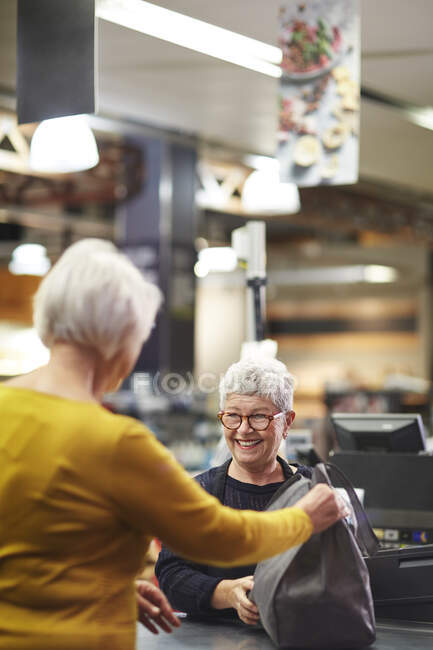 Friendly senior female cashier helping customer supermarket checkout — Stock Photo