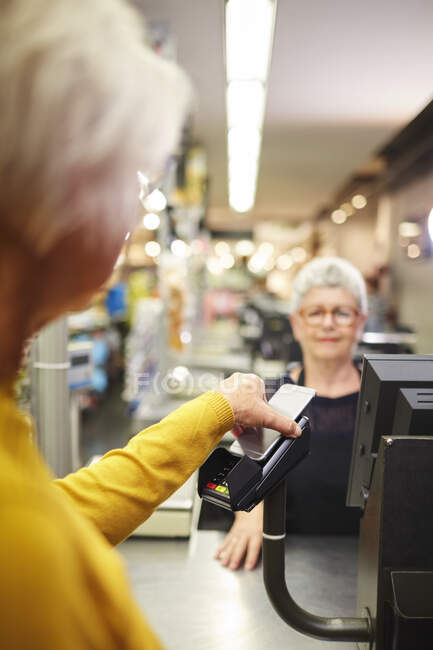 Клиент платит смартфоном на кассе супермаркета — стоковое фото