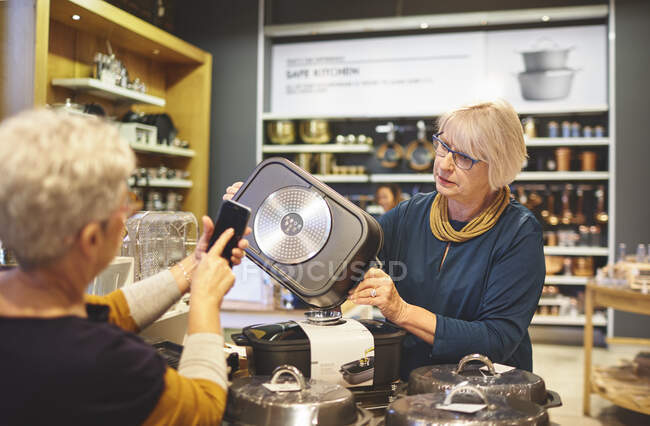 Mujeres mayores con compras de teléfonos inteligentes en la tienda de artículos para el hogar - foto de stock
