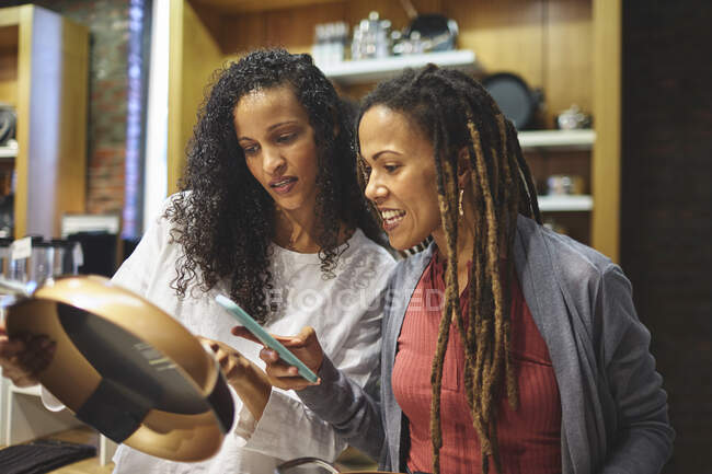 Women friends with smart phone shopping for frying pan — Stock Photo