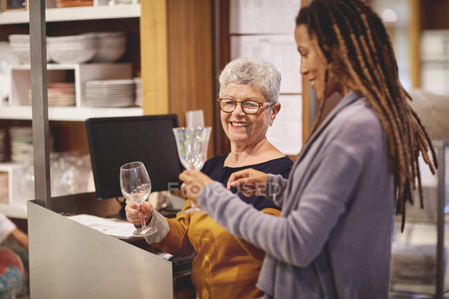 Smiling worker helping woman shopping for wine glasses — Stock Photo