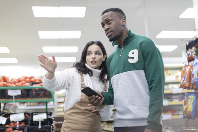 Female grocer helping male customer in supermarket — Stock Photo