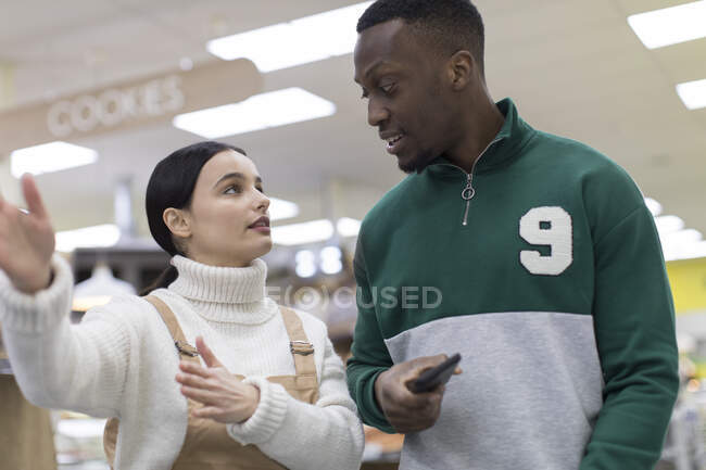 Mujer tendero ayudando a cliente masculino en el supermercado - foto de stock